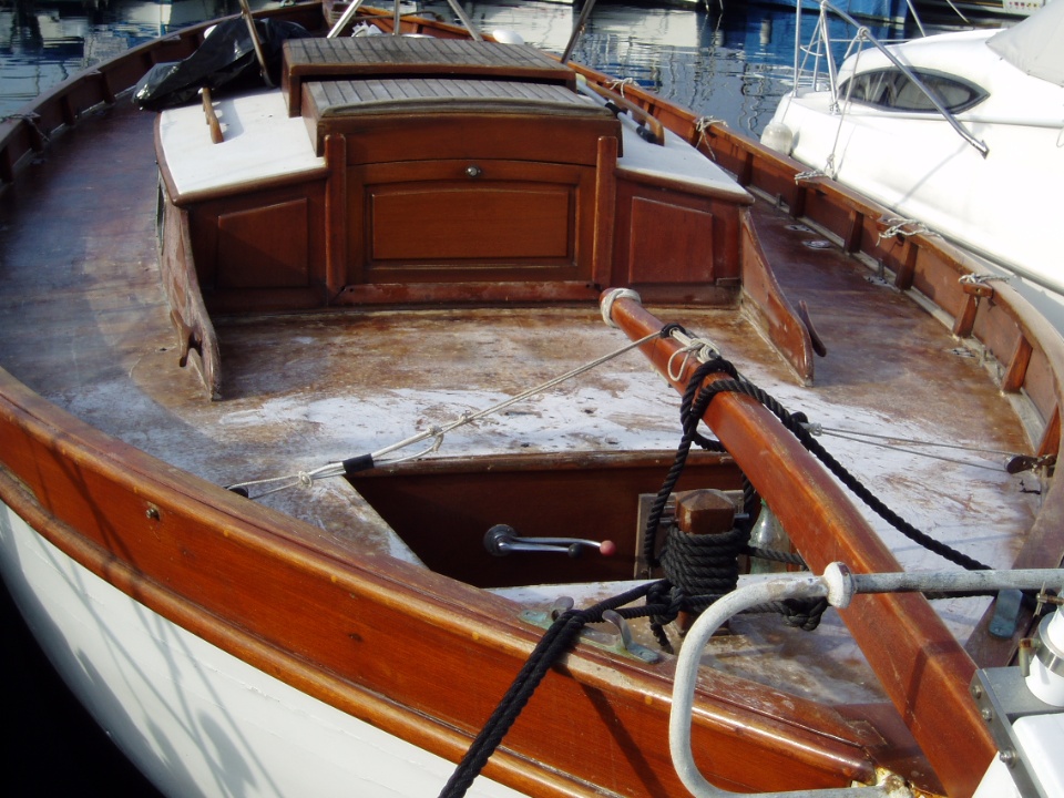 Intérieur d'un bateau en bois, montrant le pont en bois, une cabine à l'arrière et des équipements marins.