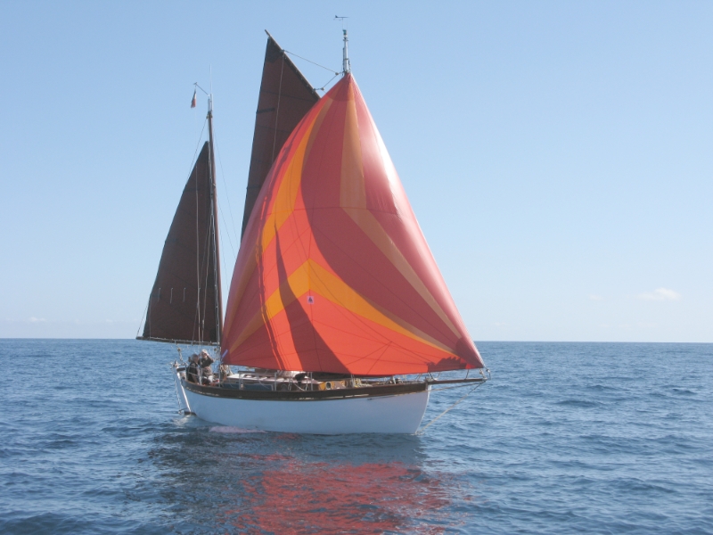 Un voilier avec des voiles colorées naviguant sur l'eau sous un ciel bleu.