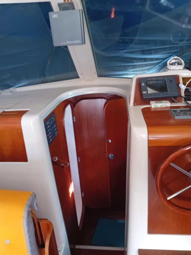 Vue intérieure d'un bateau, montrant le tableau de bord, une porte en bois et des équipements maritimes.