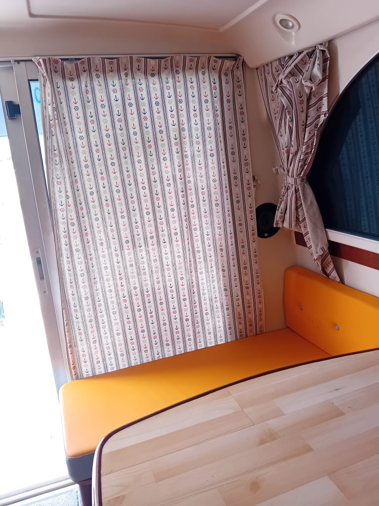 Intérieur d'un bateau avec un canapé orange et des rideaux à motif d'ancres marines.