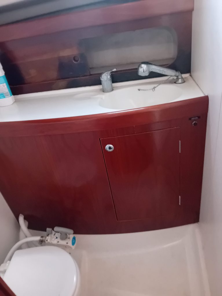 Salle de bain compacte avec lavabo et toilettes, meuble en bois et robinetterie en métal.