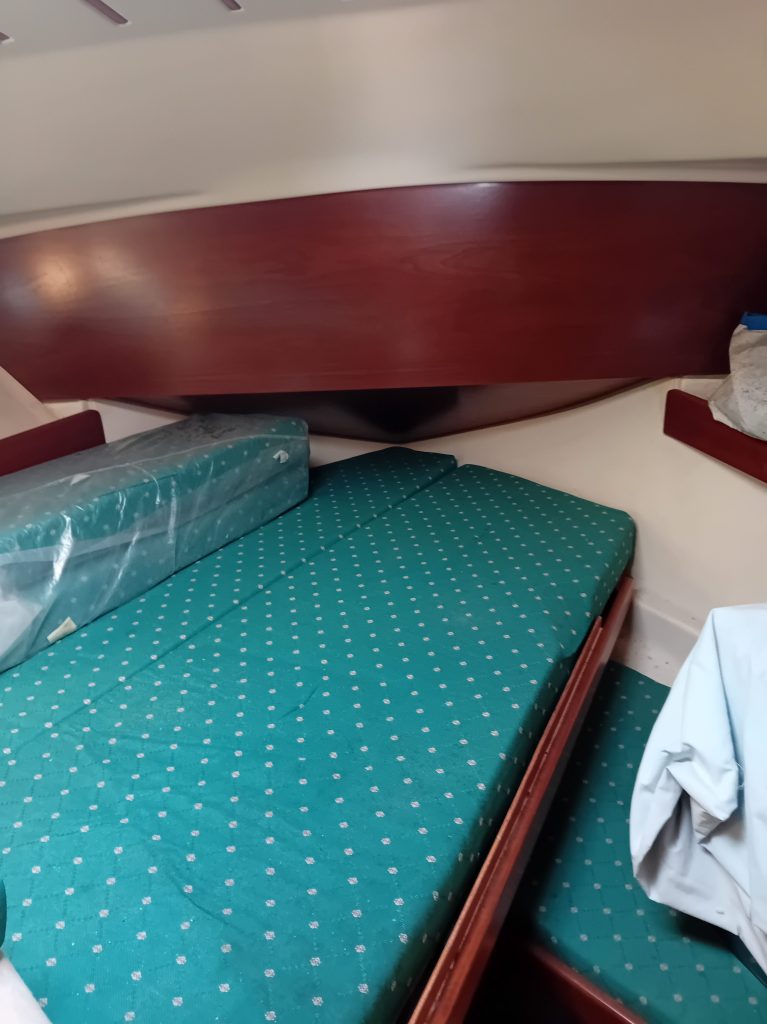 Intérieur d'un bateau avec des matelas verts à motifs, un mur en bois et un espace de rangement.