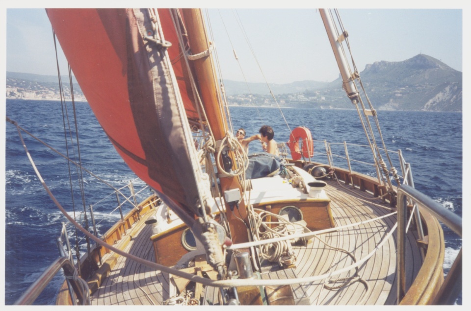Un voilier naviguant sur l'eau, avec des personnes à bord et des collines en arrière-plan.
