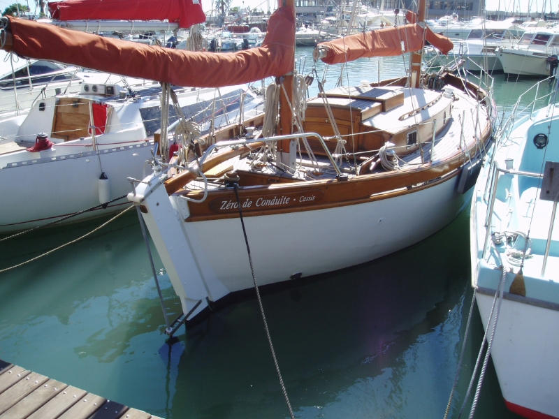 Un voilier amarré dans un port, avec une structure en bois et des voiles orange.