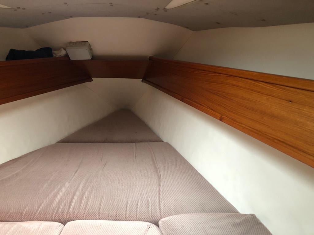 Intérieur d'un bateau avec des banquettes et des rangements en bois, mettant en évidence un espace de couchage.