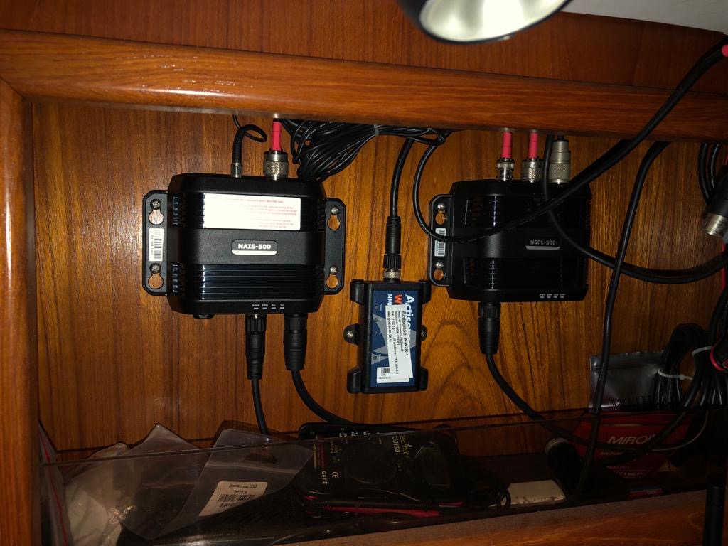 Équipements électroniques maritimes installés dans un compartiment en bois, comprenant deux boîtiers noirs avec câbles connectés.
