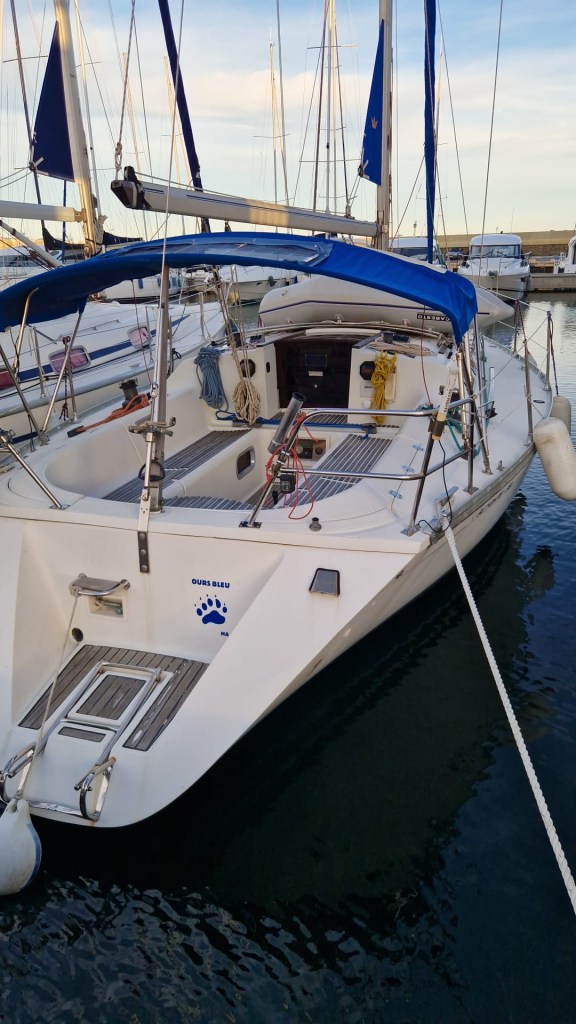 Un voilier blanc amarré dans un port, avec un toit bleu et un emblème de patte d'ours sur le côté.
