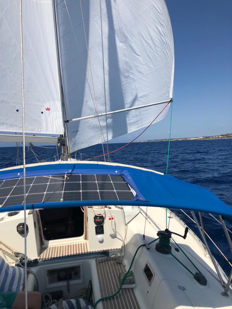 Vue sur le pont d'un voilier avec des voiles blanches, une toile bleue et un panneau solaire.