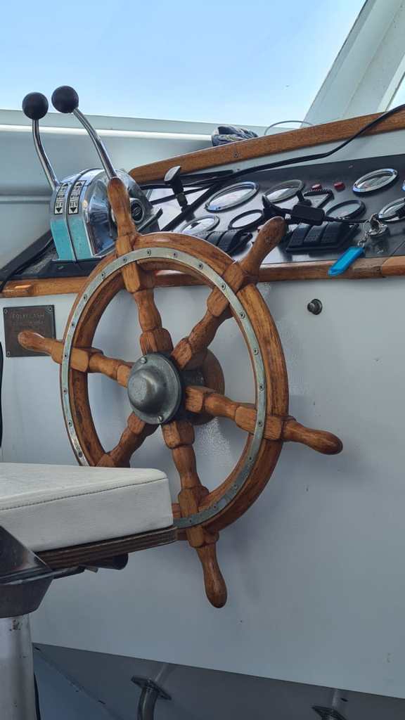 Un timon en bois monté sur le panneau de commande d'un bateau, avec des manettes et des cadrans à proximité.