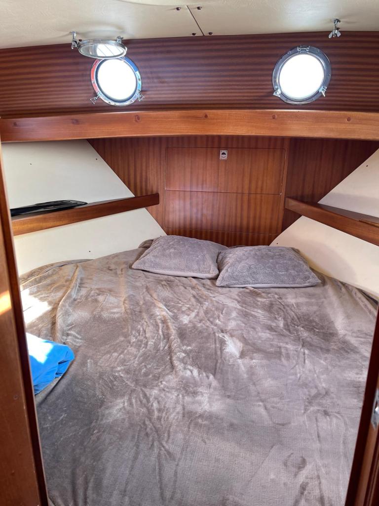 Intérieur d'une cabine de bateau avec un lit double, deux coussins et des hublots ronds.