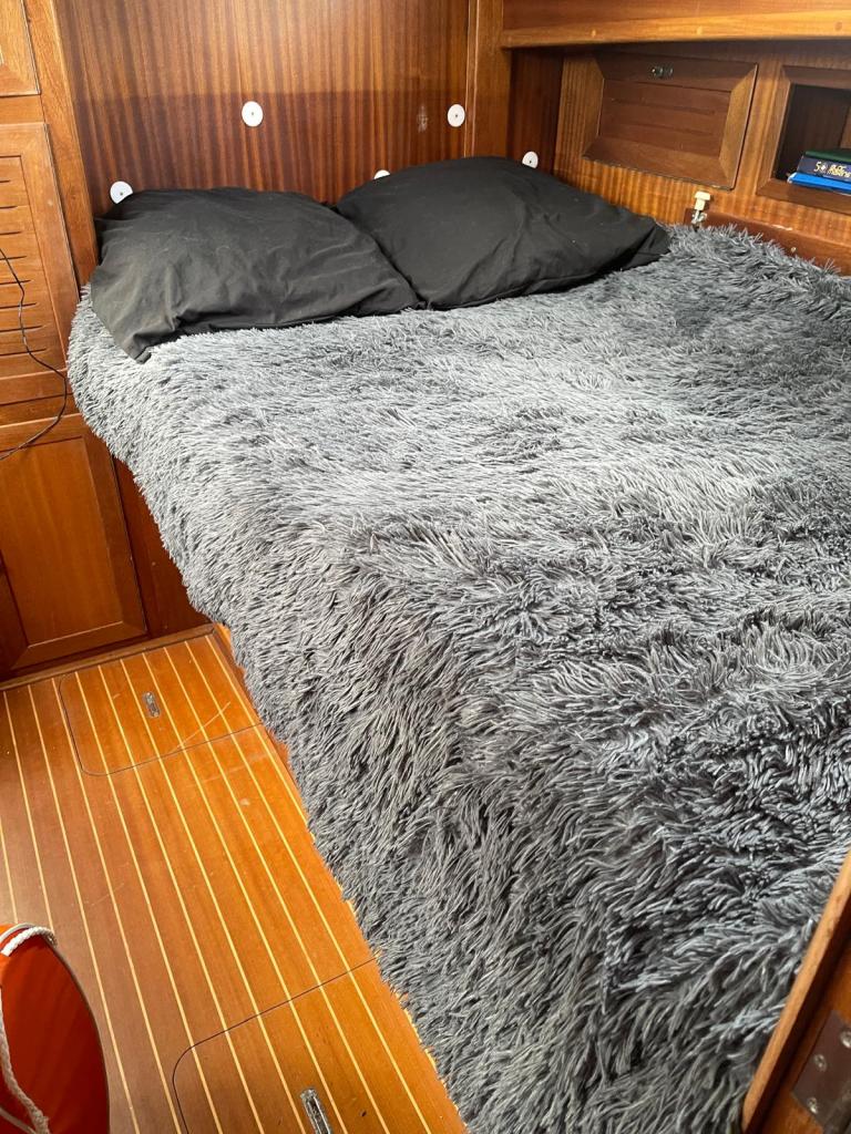 Un lit avec une couverture en fausse fourrure grise et deux oreillers noirs, situé dans un espace intérieur en bois.