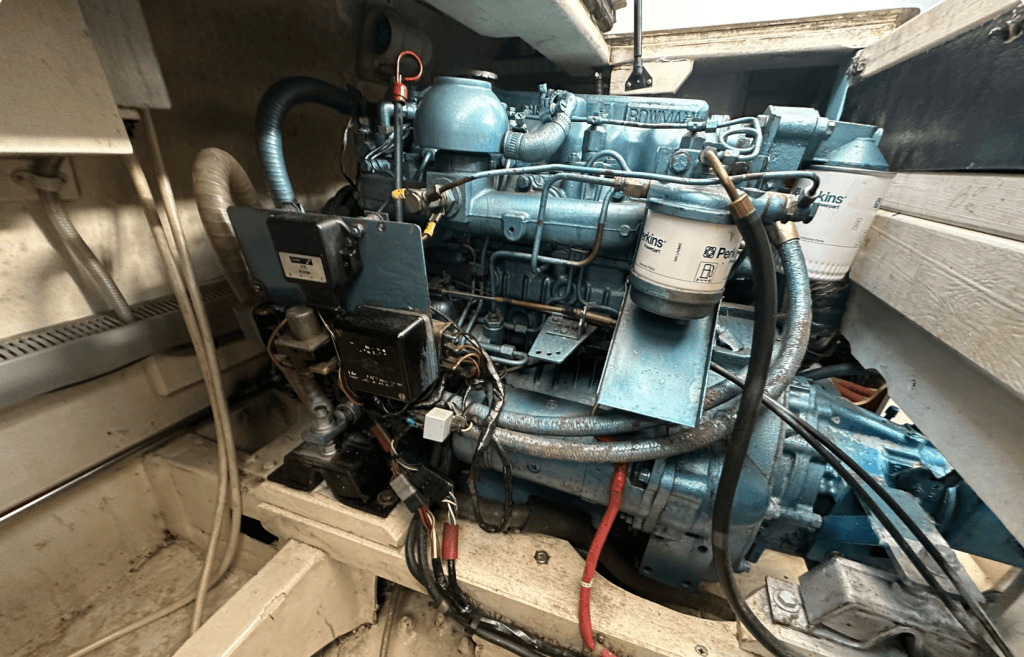 Moteur marin Perkins bleu installé dans un espace de bateau, avec des tuyaux et des câbles électriques visibles.