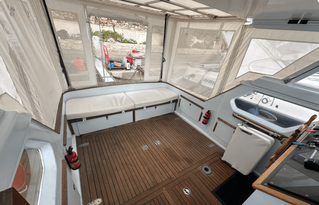 Intérieur d'un bateau avec des bancs en cuir, un sol en bois, et des murs recouverts de toile transparente laissant passer la lumière.