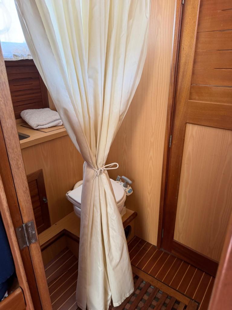 Vue d'un coin salle de bains sur un bateau, avec un rideau beige, des serviettes et des touches en bois.