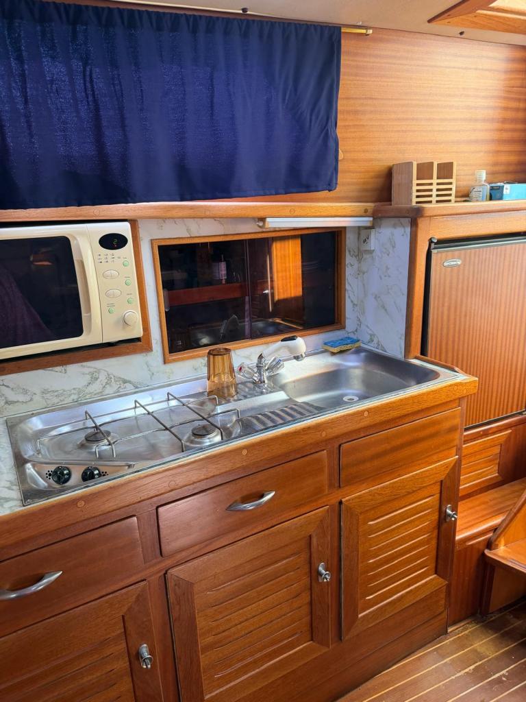 Vue d'une cuisine de bateau avec un évier en acier inoxydable, une cuisinière à gaz, un four à micro-ondes et des armoires en bois.